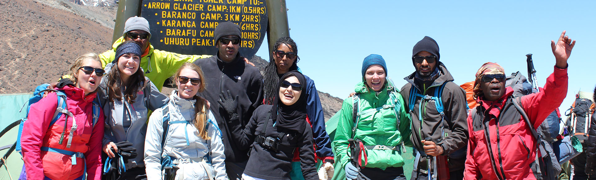 Climbing group and guides celebrating beside the Lava Tower Camp trail sign