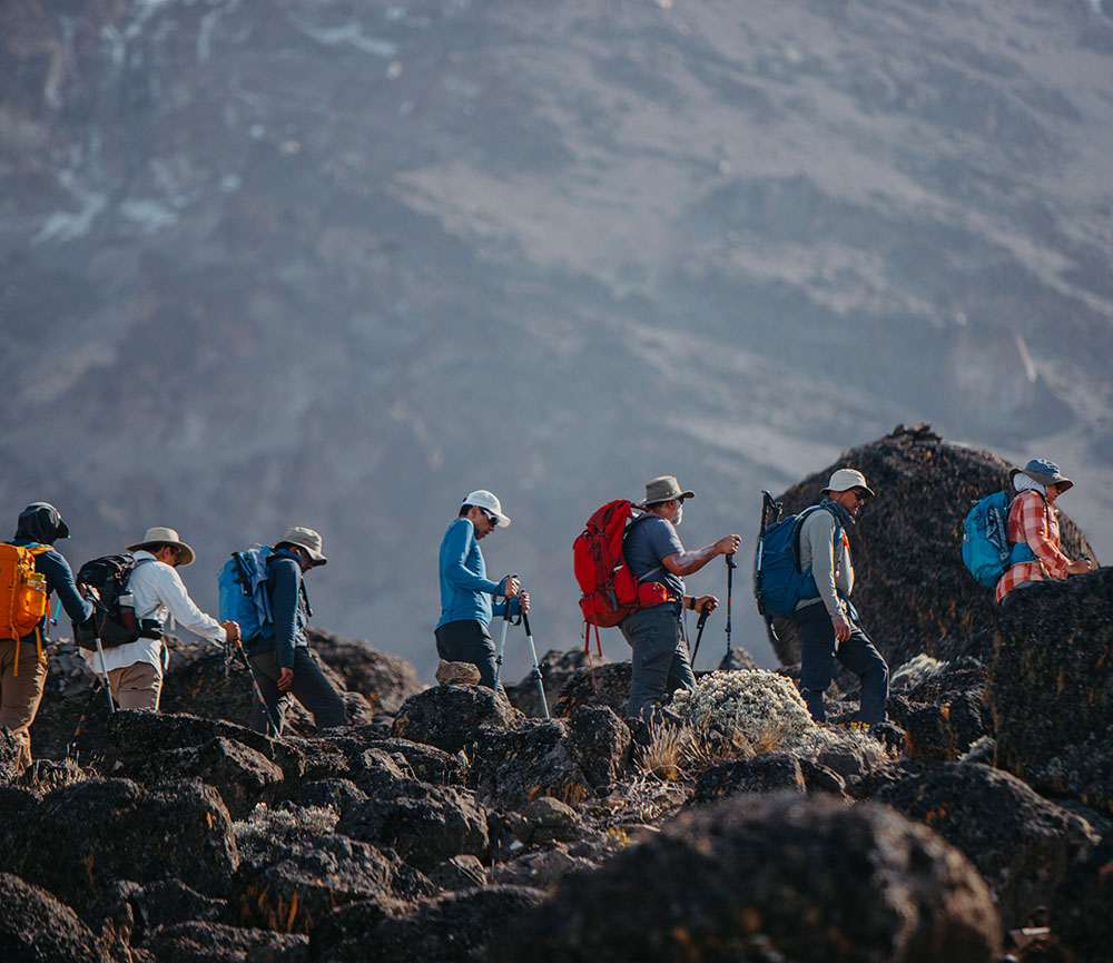 Trekkers with backpacks crossing a rocky volcanic landscape below the peak