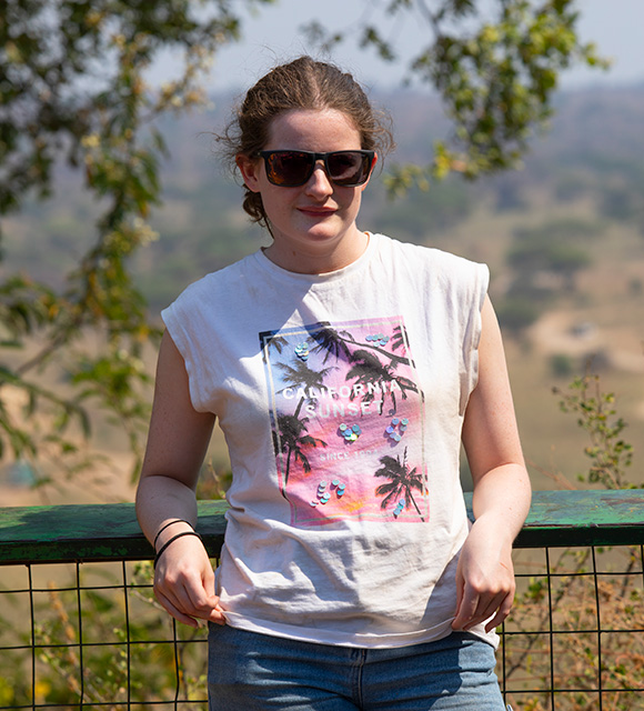 Traveller in sunglasses leaning on a wooden railing with the Tanzanian savannah behind