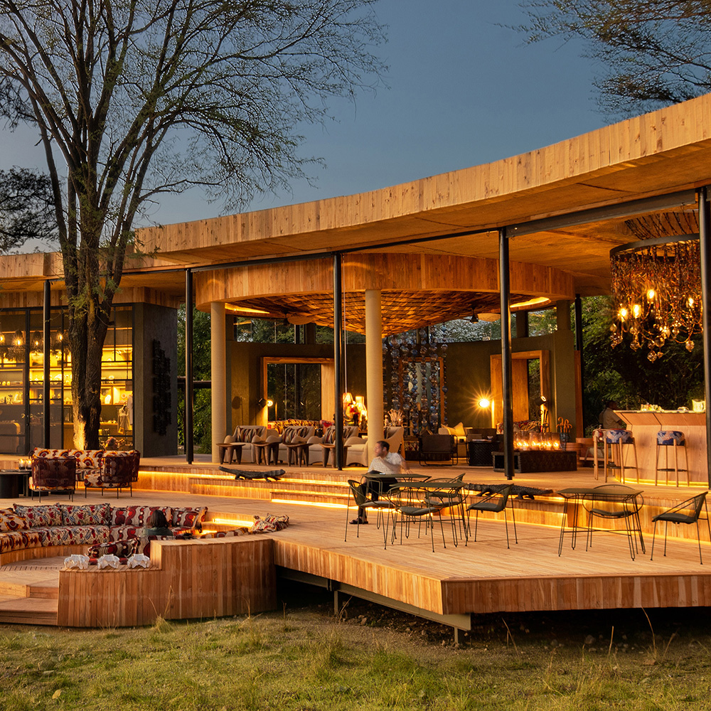 Open-sided timber safari lodge lounge and fire pit lit up at dusk in the Serengeti