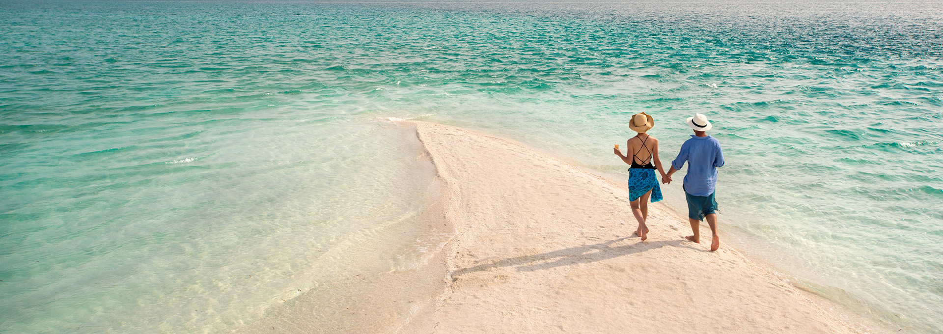 Couple walking on a pristine white sandbar in the turquoise waters of Zanzibar